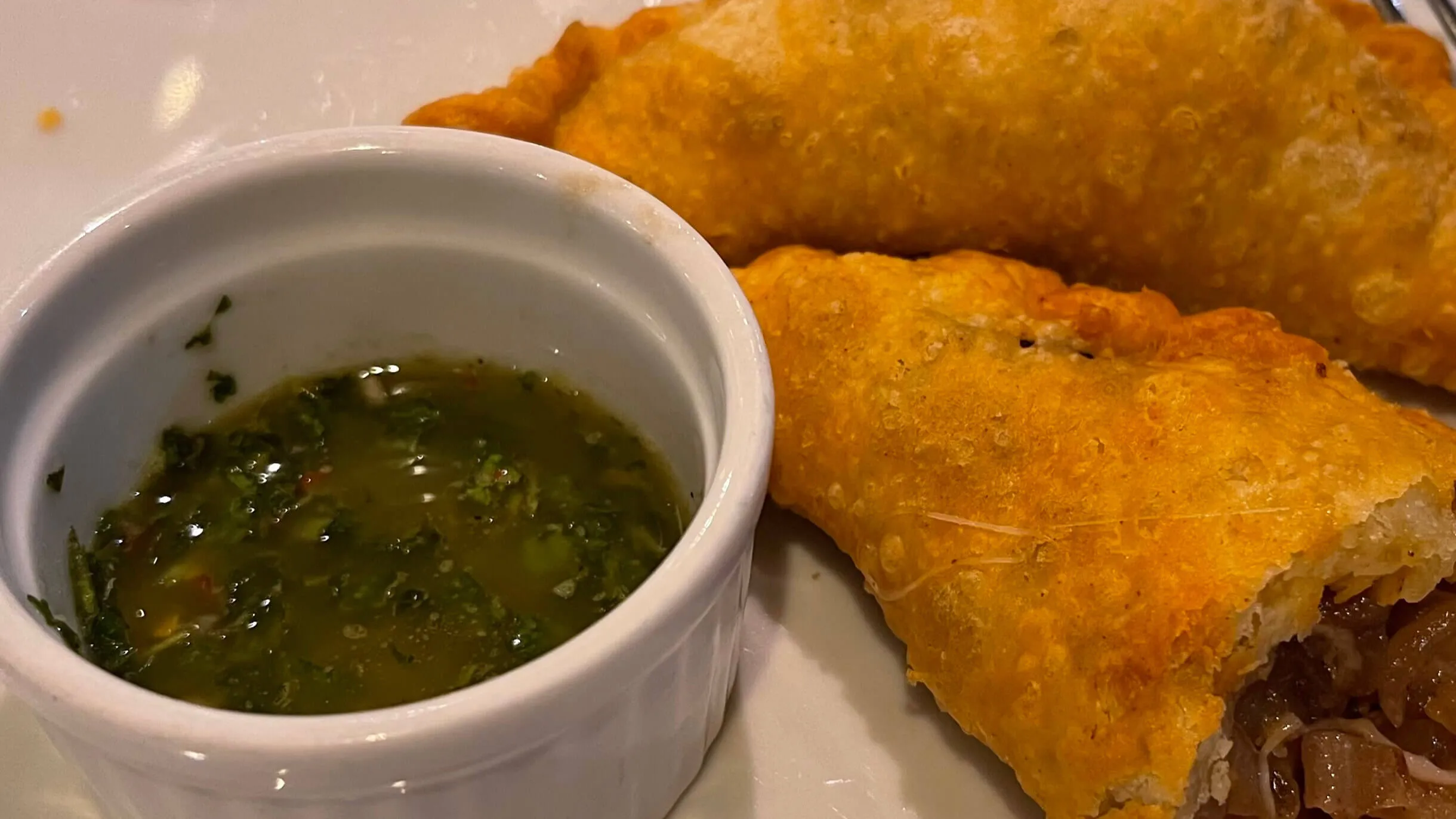 Deep-fried empanadas with a side of chimichurri sauce.